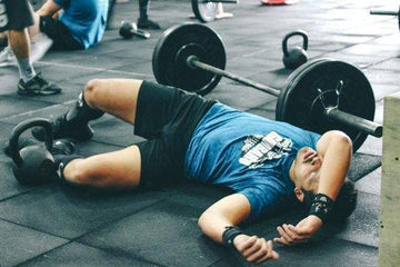 Tired man lying on gym floor after intense weightlifting session with barbell and kettlebell nearby
