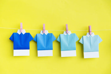 Origami paper shirts in varying blue shades clipped on a string against yellow background