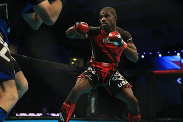 MMA fighter in red and black Green Hill gear with red gloves in fighting stance inside cage arena