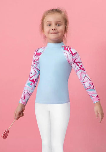 Young girl in blue and pink marbled long-sleeve top with white leggings on a pink background