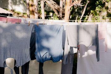 Grey and blue long-sleeve shirts hanging on clothesline outdoors in sunny garden drying naturally