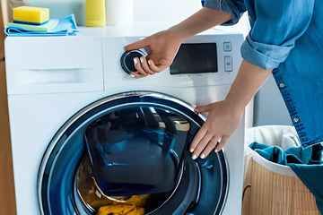 Person in blue shirt operating a front-loading washing machine with laundry basket nearby