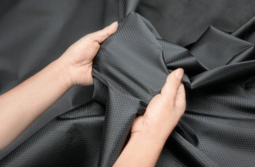 Hands holding and stretching black polyester fabric with a subtle grid pattern
