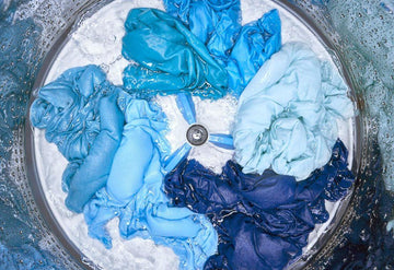Blue clothes soaking inside a washing machine drum filled with water during laundry