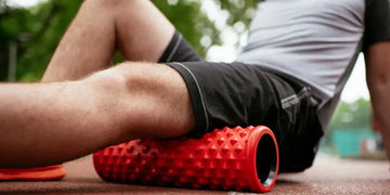 Athlete using a red textured foam roller for leg muscle recovery on outdoor track