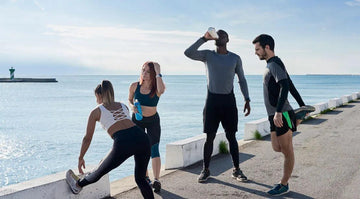 Group of four diverse people stretching and hydrating by the sea during outdoor workout